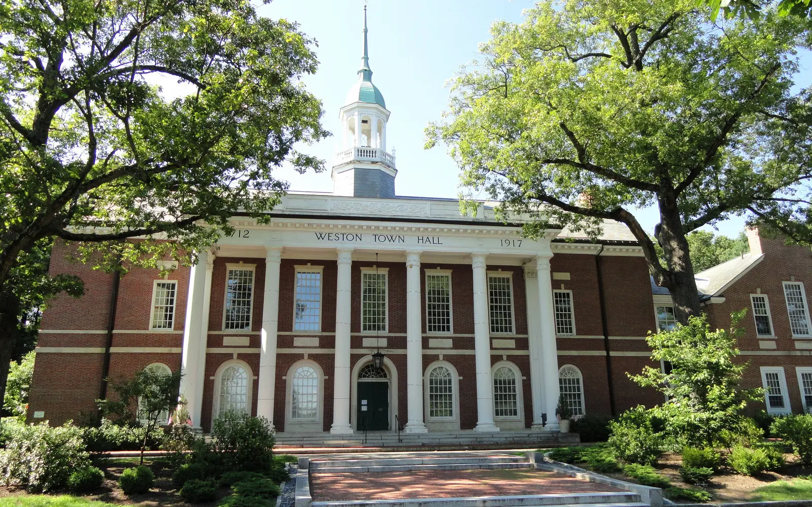 Weston Town Hall, a brick building with a white columned portico and cupola, among trees